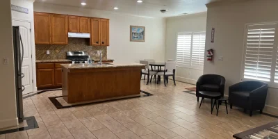 Modern kitchen with wooden cabinets, center island, dining table, and cozy seating area at AJ Residential Care Home, Fresno, CA.