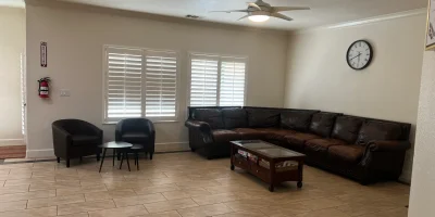 Large living room with brown leather sectional sofa, chairs, coffee table, ceiling fan, and wall clock in Fresno care home.