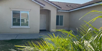 Close-up view of care home entrance in Fresno with tiled roof, white door, and lush green plants in the front yard.